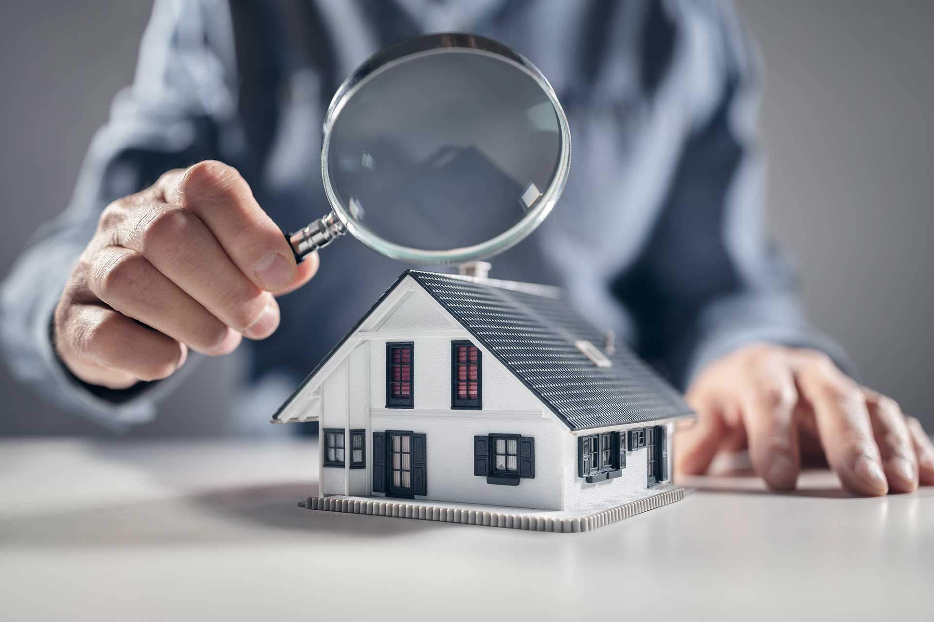 Magnifying glass over a model house, symbolizing Pro Mosquito Solutions’ comprehensive free inspections to identify and eliminate pest problems in Rhode Island and Southeastern MA.