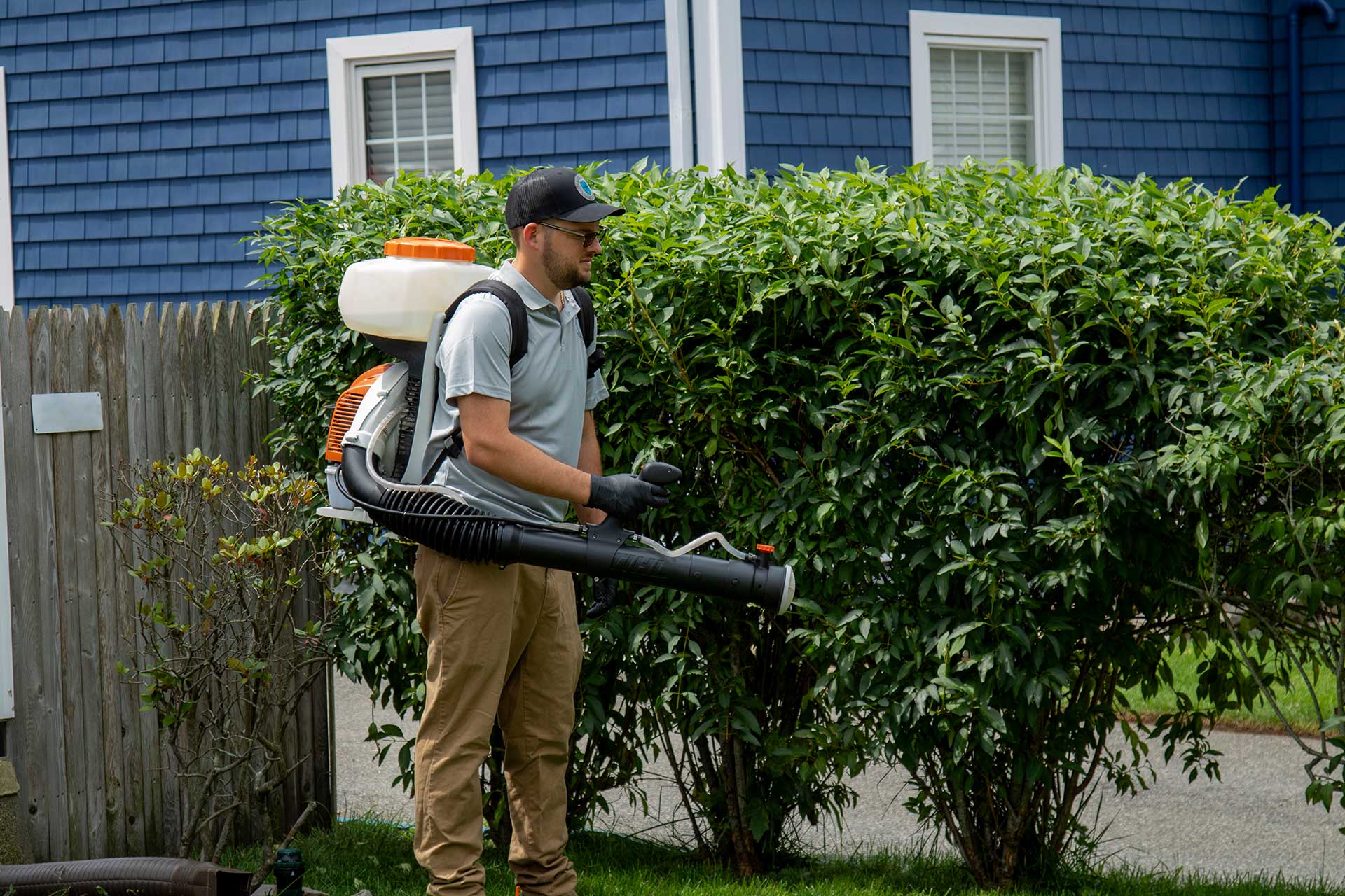 Pro Mosquito Solutions technician in Rhode Island applying mosquito and tick barrier treatment with a professional sprayer for effective pest control.