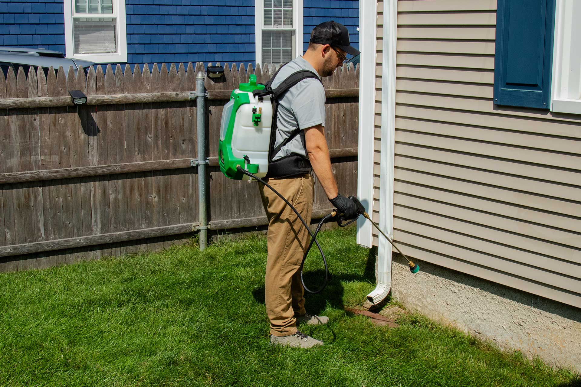 Pro Mosquito Solutions technician in uniform using a professional foundation sprayer to apply a comprehensive barrier treatment for pest control in Rhode Island and Southeastern MA.