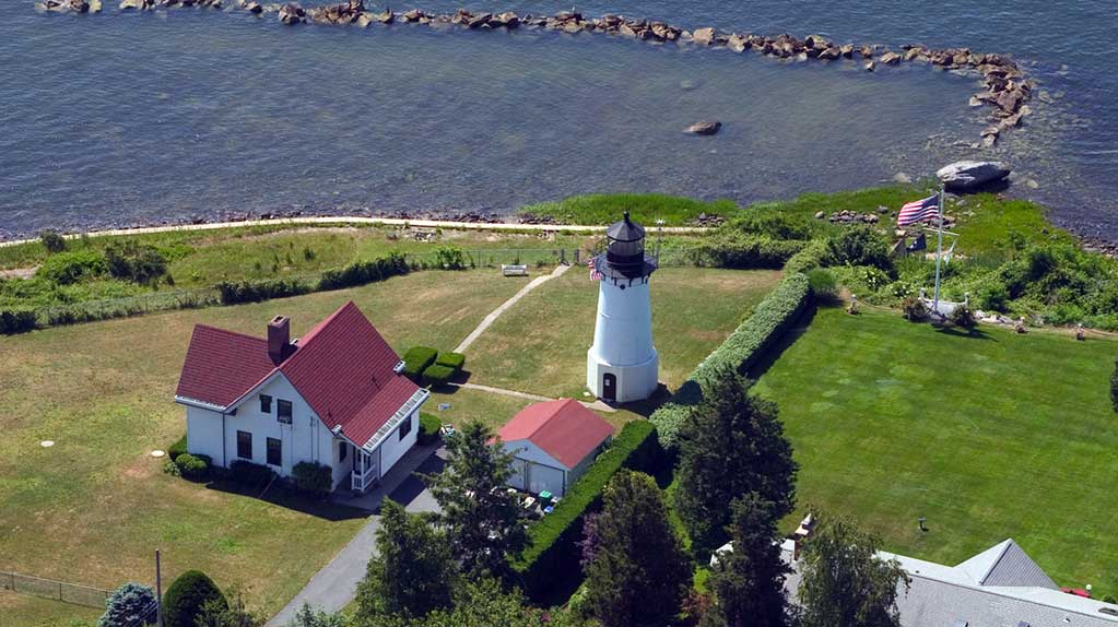 Warwick Neck Lighthouse in Rhode Island, a white tower with red roof perched on grassy hill overlooking Narragansett Bay, within Pro Mosquito Solutions service area.