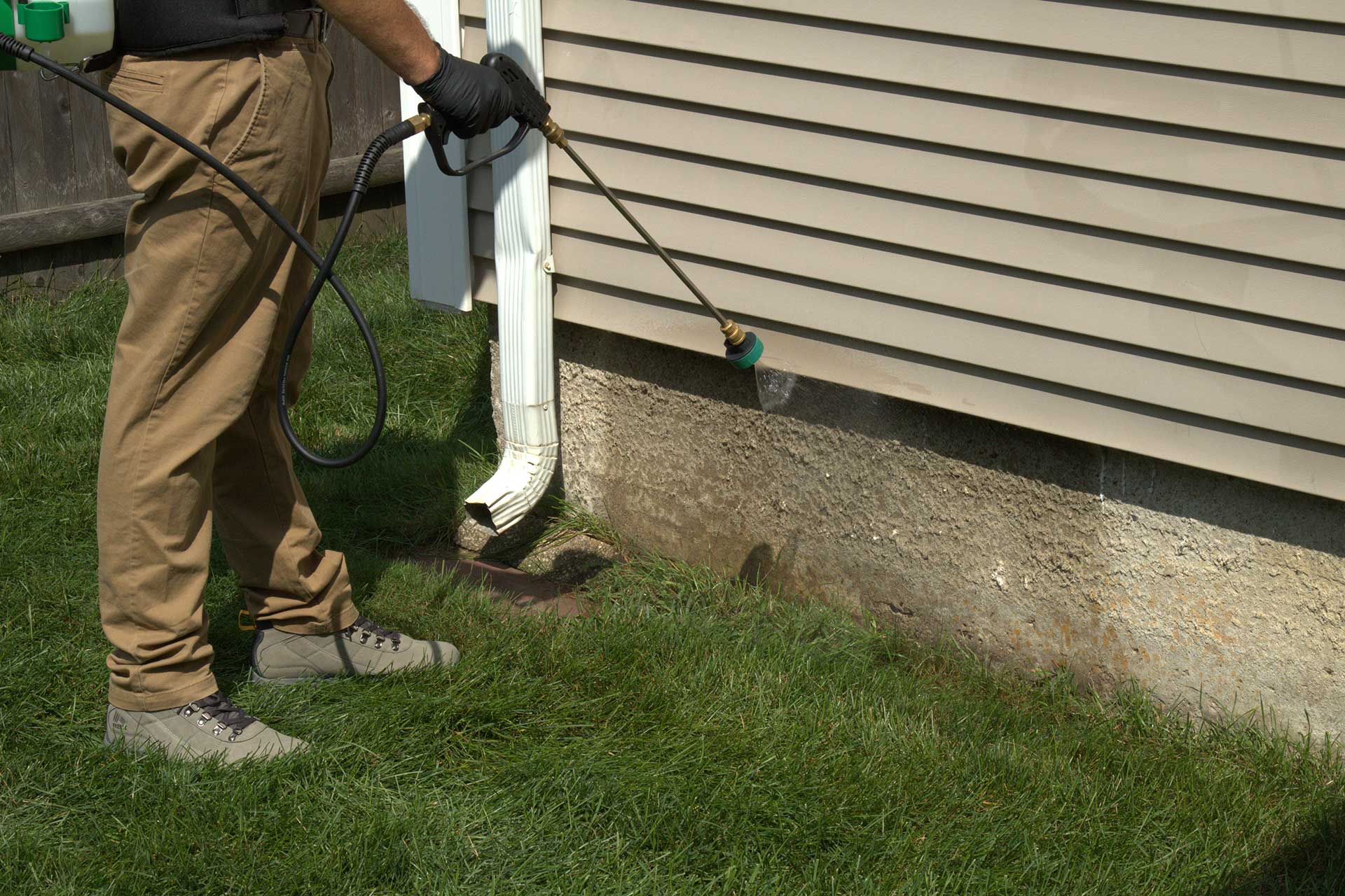 Pro Mosquito Solutions technician applying an ant foundation barrier treatment around a Rhode Island property, protecting against crawling pests like ants.
