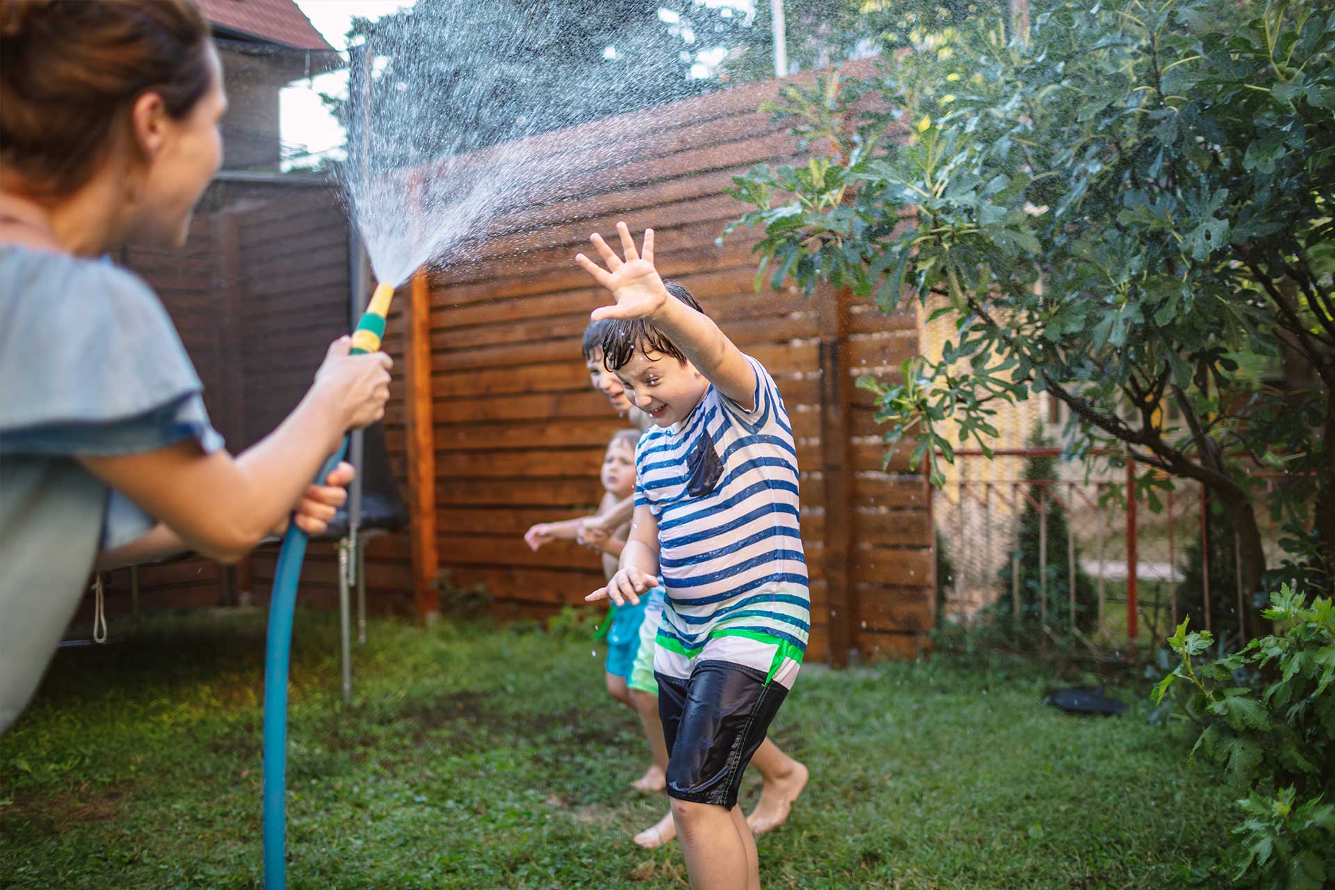 Three children and a woman enjoying water play with a garden hose sprinkler, highlighting outdoor family fun in a pest-free yard maintained by Pro Mosquito Solutions.