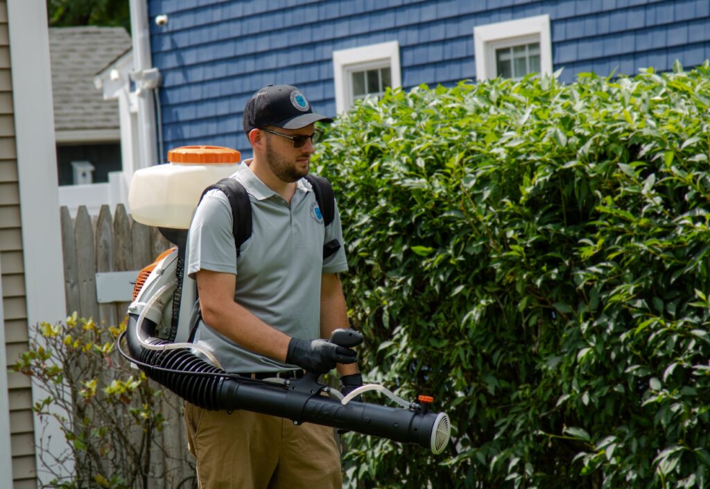 Pro Mosquito Solutions technician spraying a Rhode Island yard for mosquitoes and ticks with professional equipment, ensuring lawn and outdoor space protection.