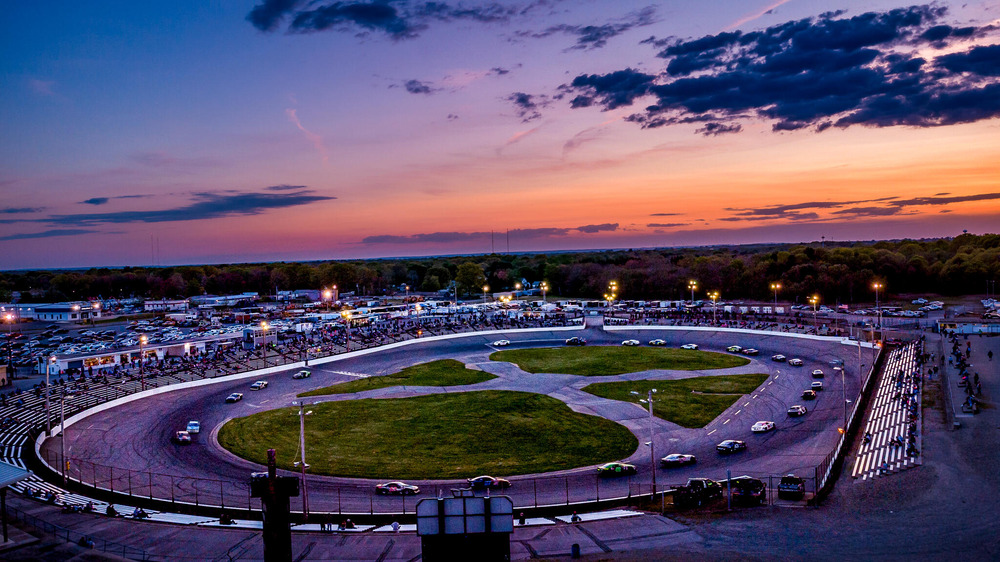 Aerial view of Seekonk Speedway at sunset, with the racetrack illuminated by the warm glow of the setting sun against a vibrant sky.