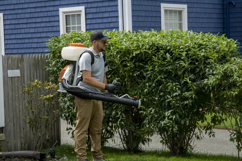 Pro Mosquito Solutions technician in Rhode Island applying mosquito and tick barrier treatment with a professional sprayer, ensuring a safe, pest-free yard.