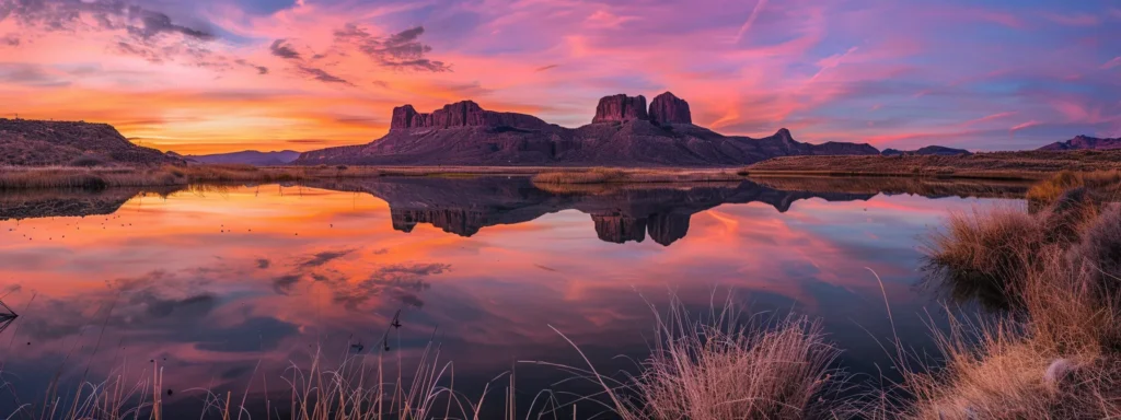 a serene landscape at dawn, where vibrant orange and pink hues paint the sky above a tranquil lake reflecting the silhouettes of distant mountains.